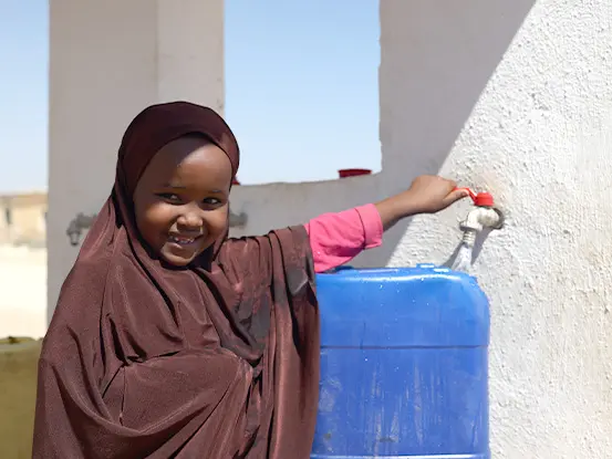A young girl in Somalia smiling as she fills her water container from a clean water tap provided by Islamic Relief