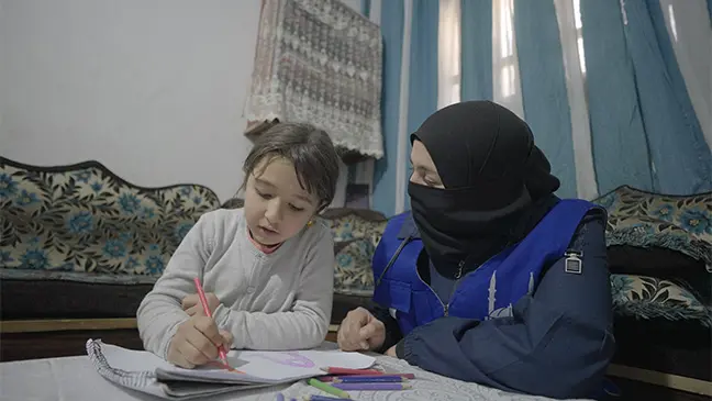 An Islamic Relief worker in Syria supports a young orphaned girl as she writes